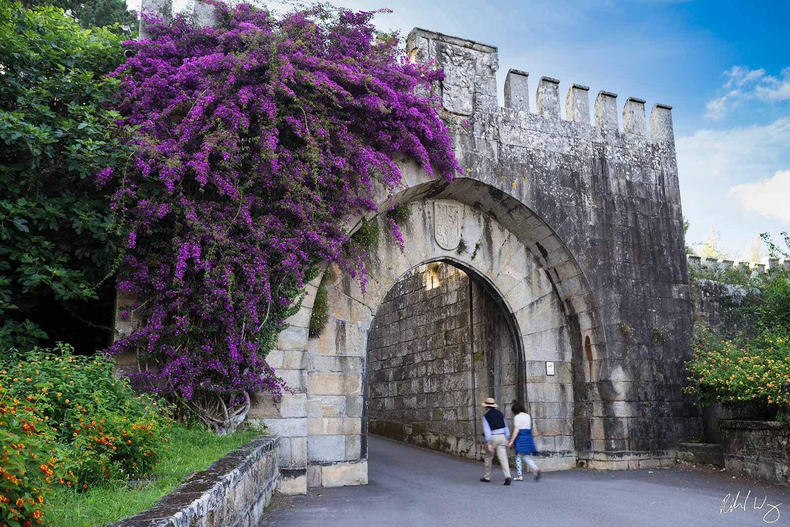 Male & Female Couple Holding Hands Walking Under Arch at Parador de Baiona, Baiona, Spain